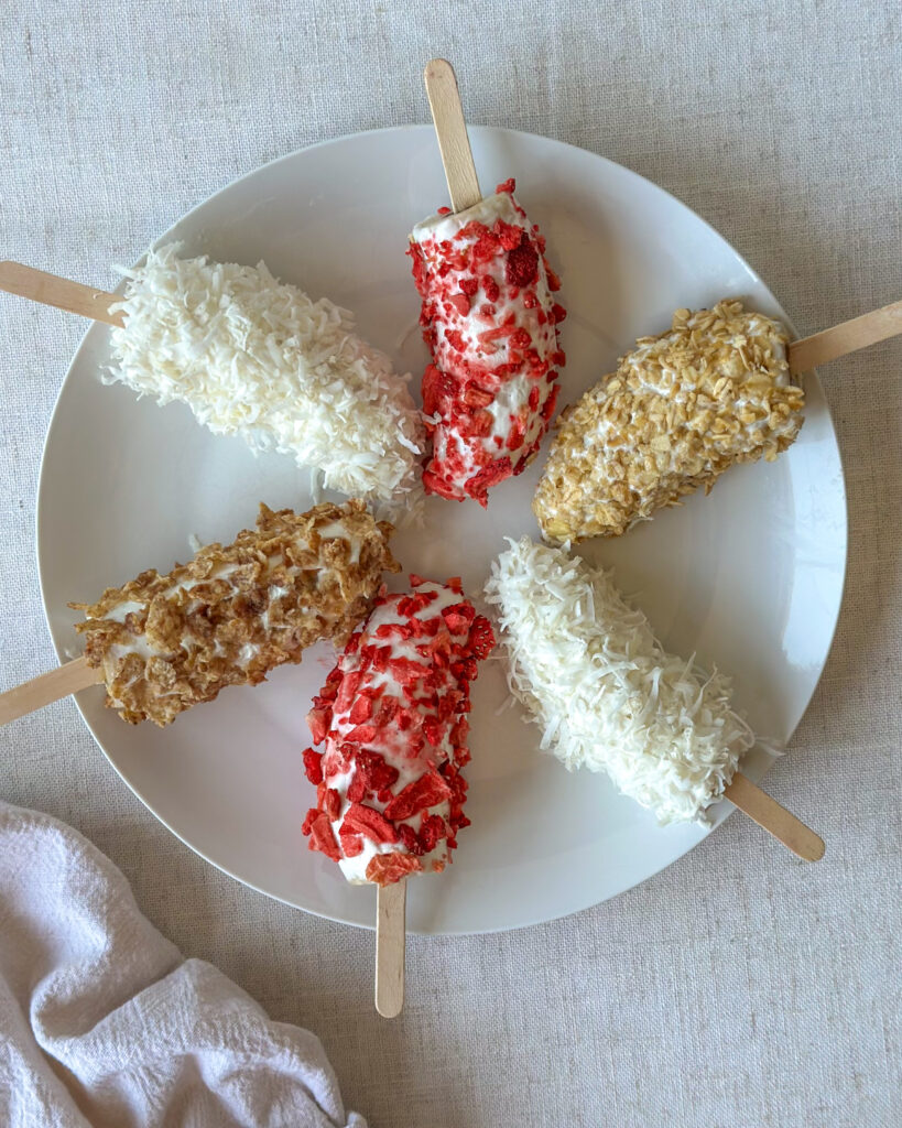 Frozen Greek yogurt banana pops arranged in a spiral pattern on a white plate with a neutral-colored napkin