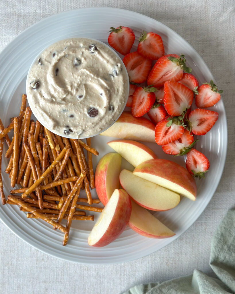 Overhead view of swirled high-protein cookie dough dip surrounded by fresh fruit, pretzels, and other dippers