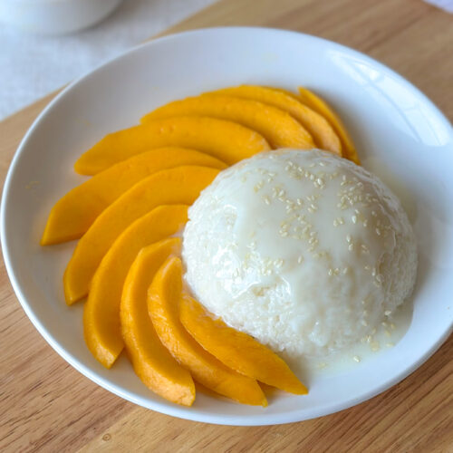 Mango sticky rice served with a spherical mound of sticky rice and fresh mango slices in a shallow white bowl.