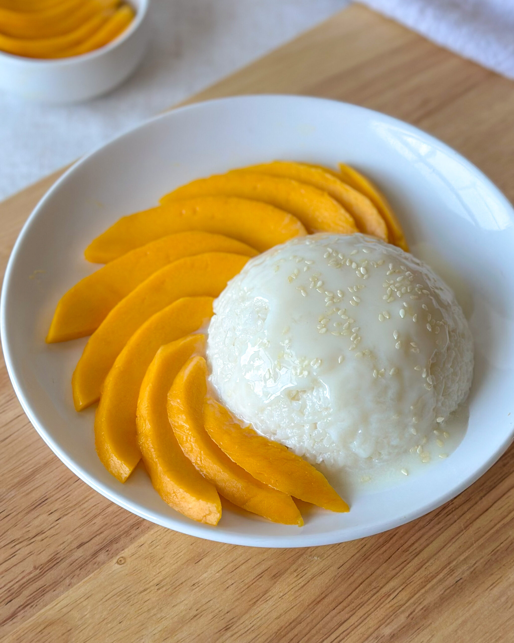 Mango sticky rice served with a spherical mound of sticky rice and fresh mango slices in a shallow white bowl.