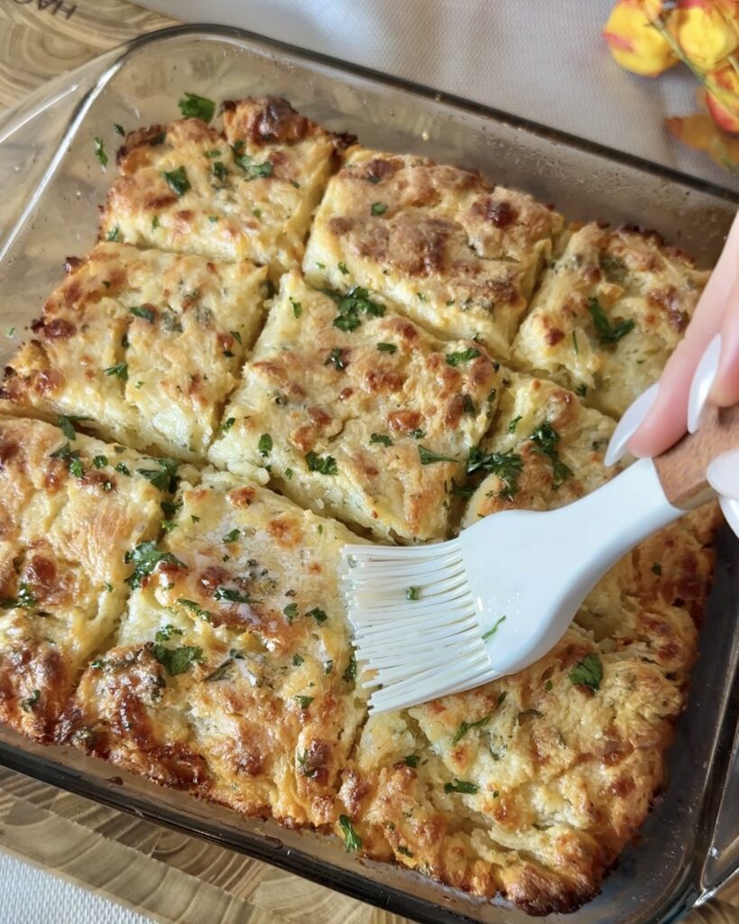 Hand brushing garlic butter over freshly baked Cheddar Bay swim Biscuits