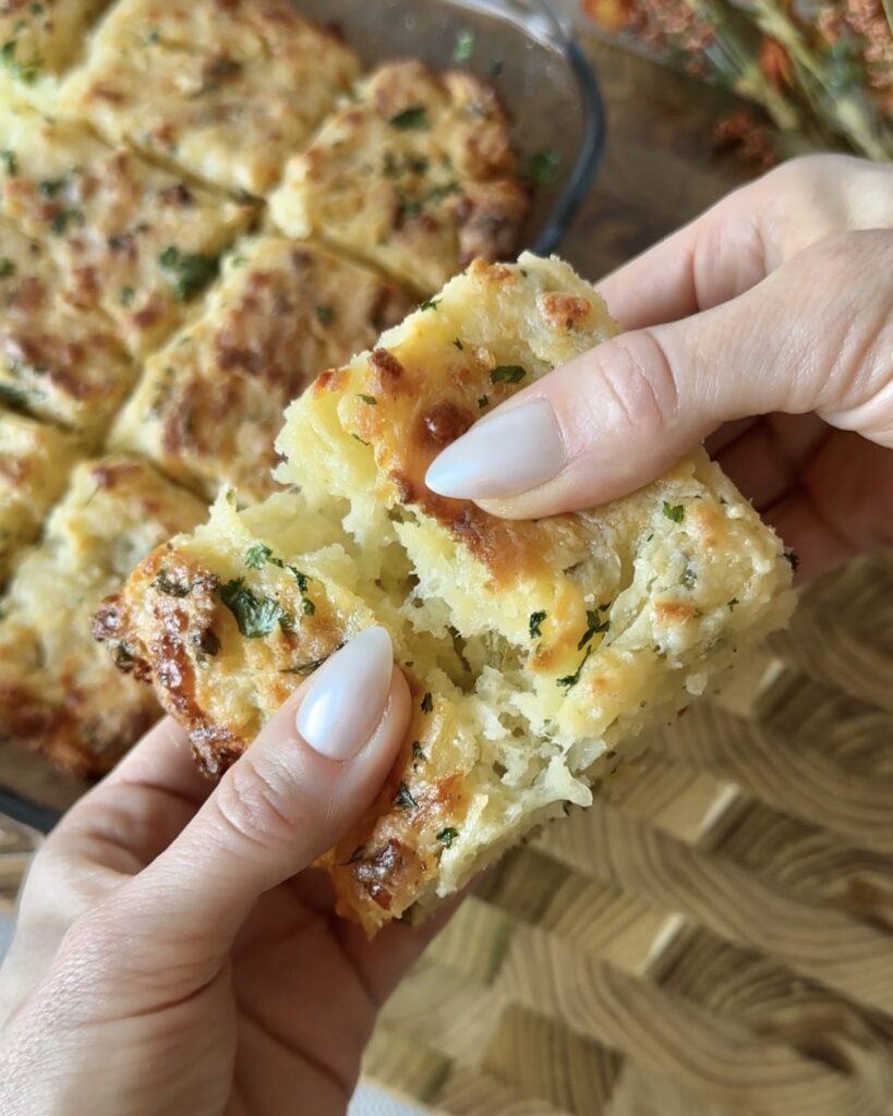 Hand pulling apart a homemade Cheddar Bay swim Biscuit to show the tender interior and melted cheddar cheese