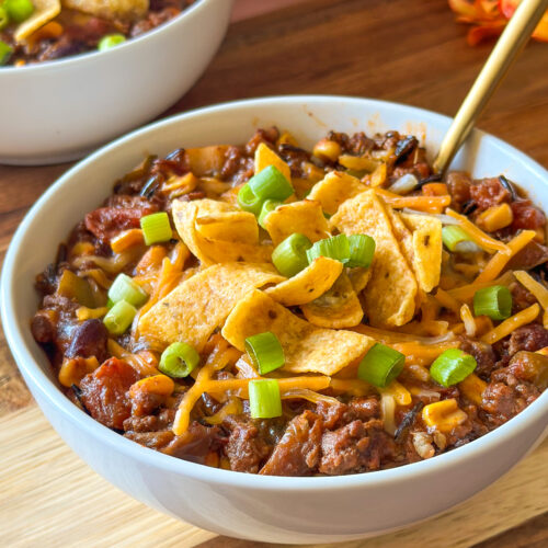Front view of a bowl of homemade chili with a spoon and another bowl of chili in the background