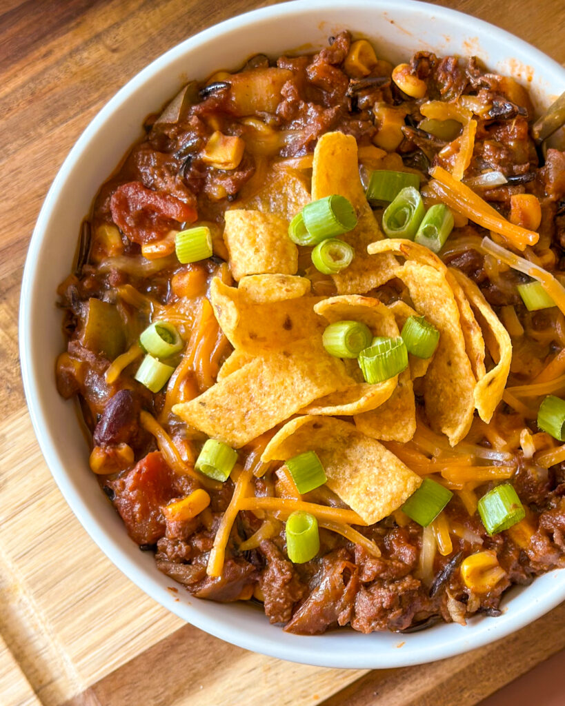 : Extreme close-up of hearty homemade chili topped with melted cheese, corn chips, and green onion