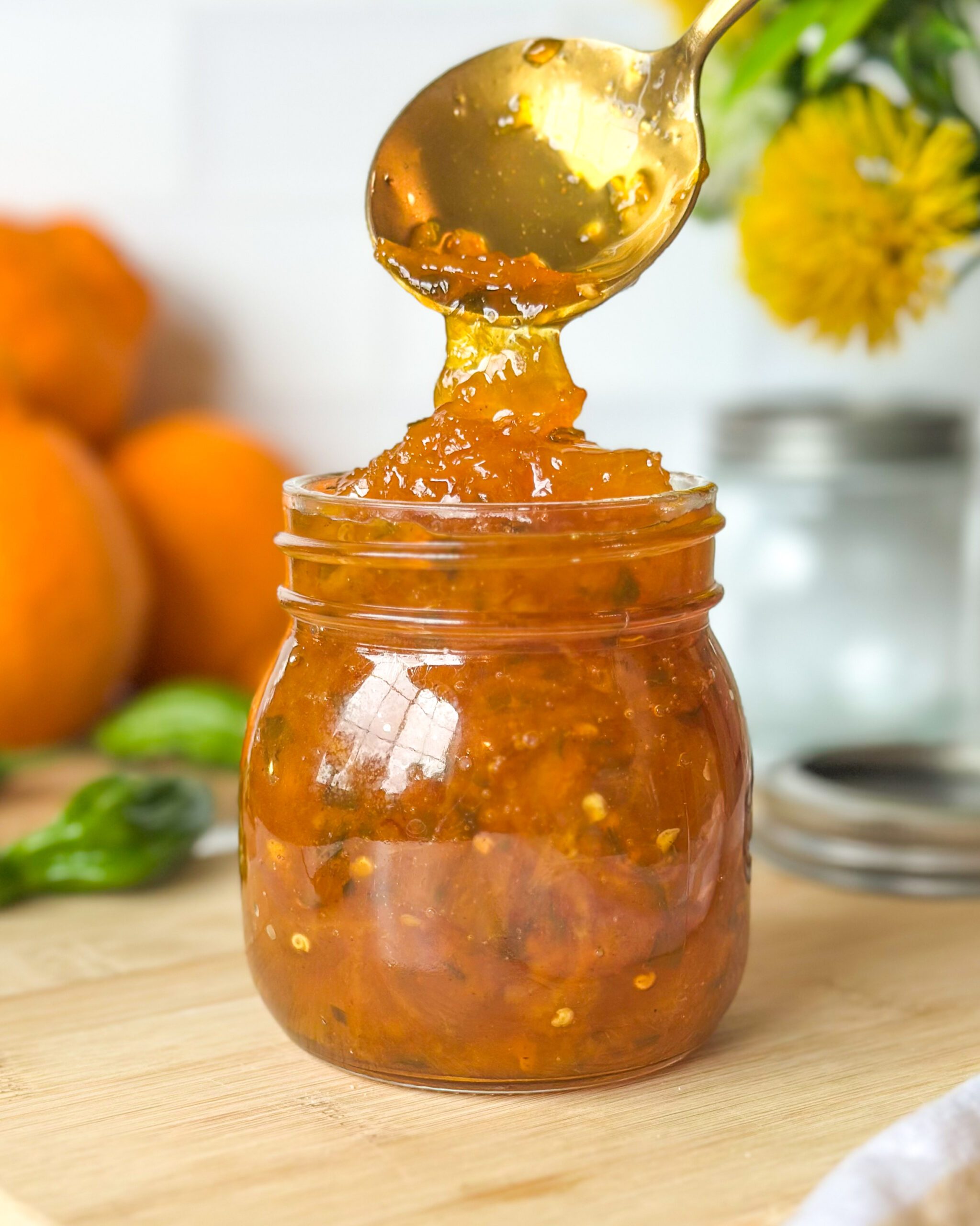 Spoon spooning spicy citrus pepper jelly into a glass jar, highlighting the thick glossy texture of the jelly