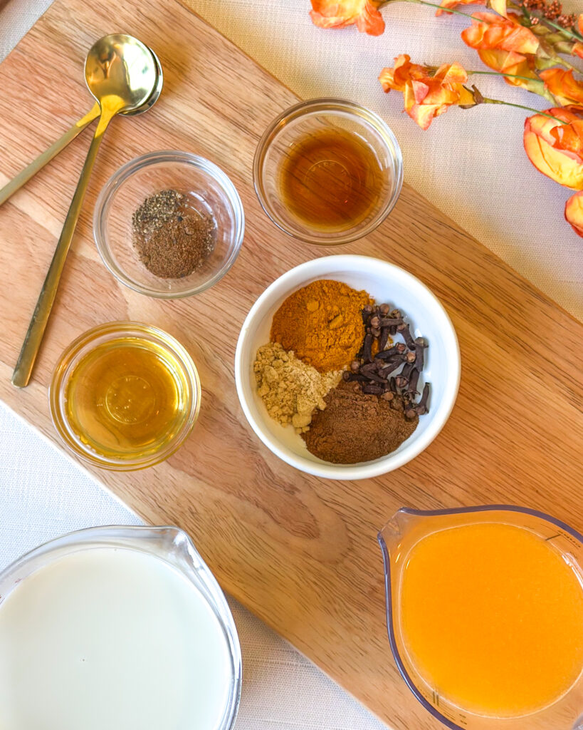 Golden milk ingredients arranged in a flat lay with oat milk, Sumo citrus juice, turmeric, ginger, cinnamon, cloves, nutmeg, vanilla and honey