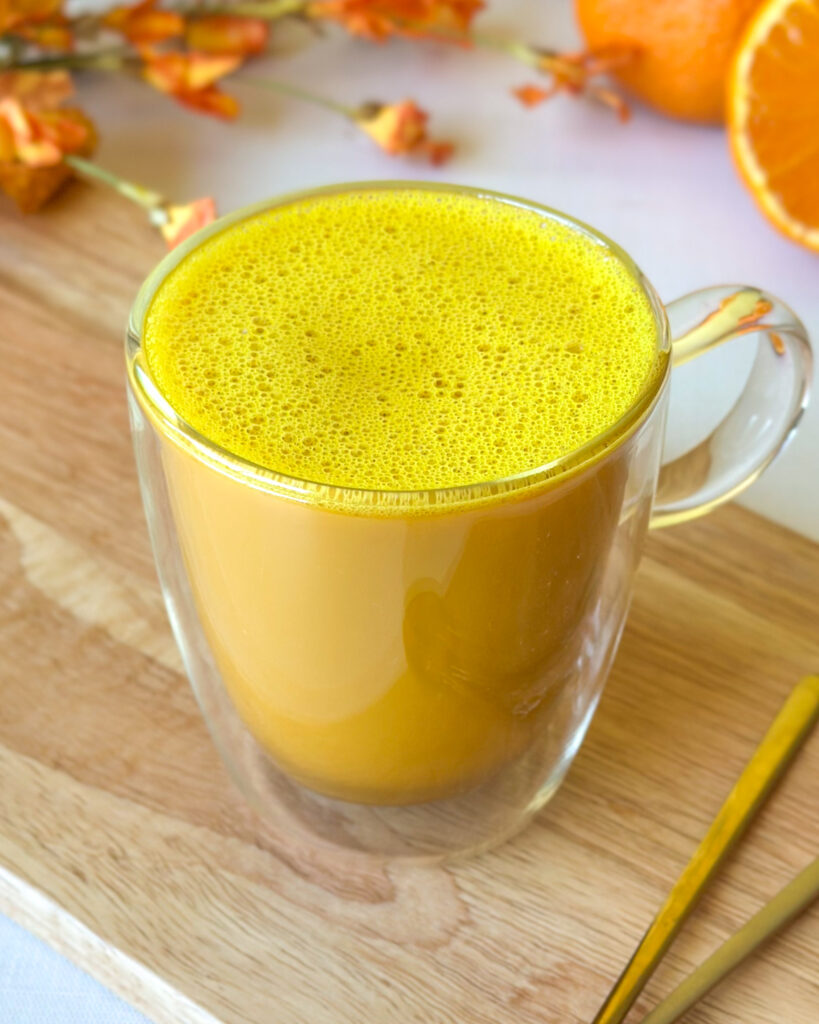 Golden milk turmeric latte with frothy top served alongside sliced Sumo citrus, flowers and a golden spoon