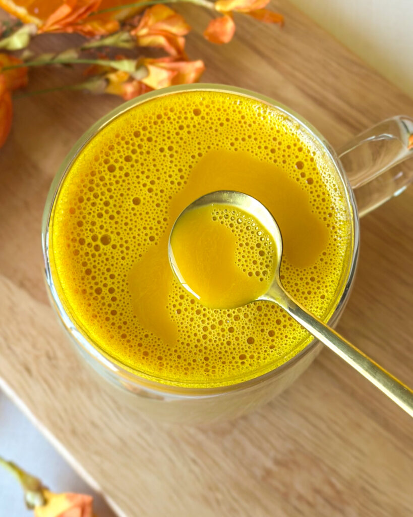 Overhead view of golden milk latte with frothy topping as a spoon reveals its golden color and creamy texture