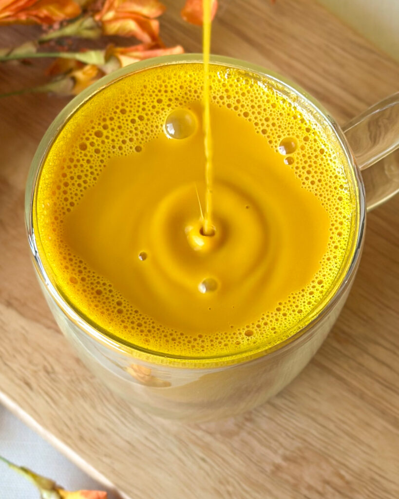 Drips cascading and splashing into a golden milk turmeric latte, creating bubbles and droplets across the frothy surface