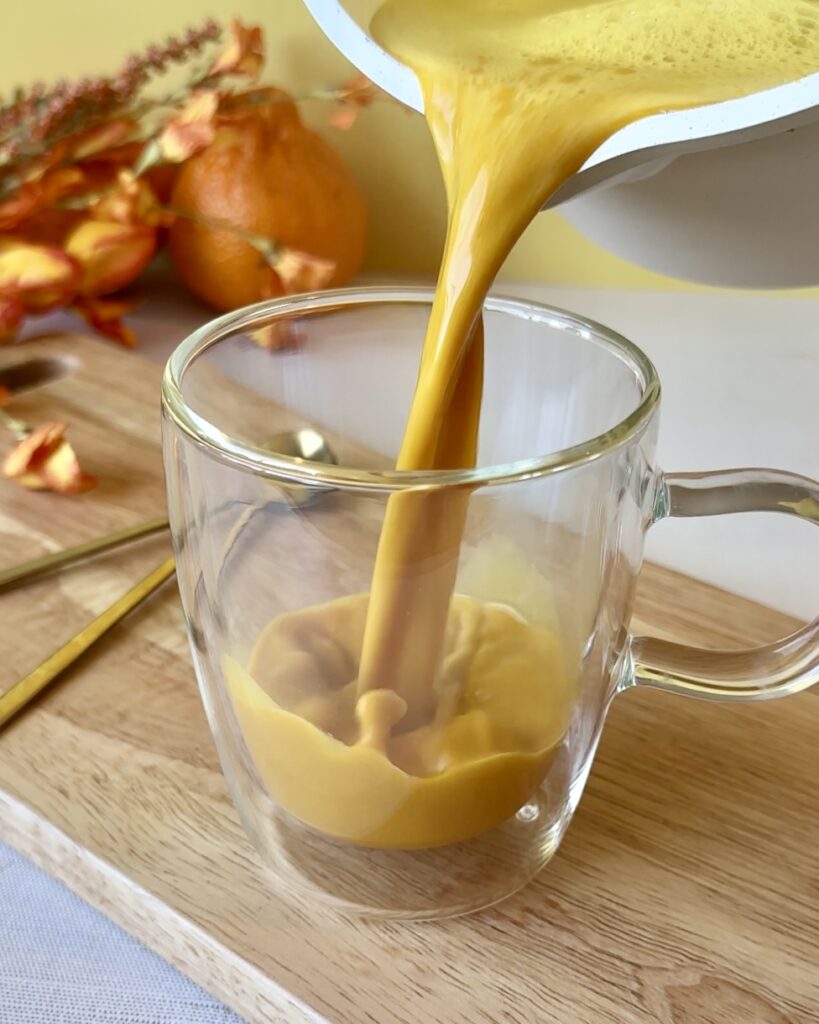 Pouring golden milk turmeric latte from a saucepan into a glass mug.