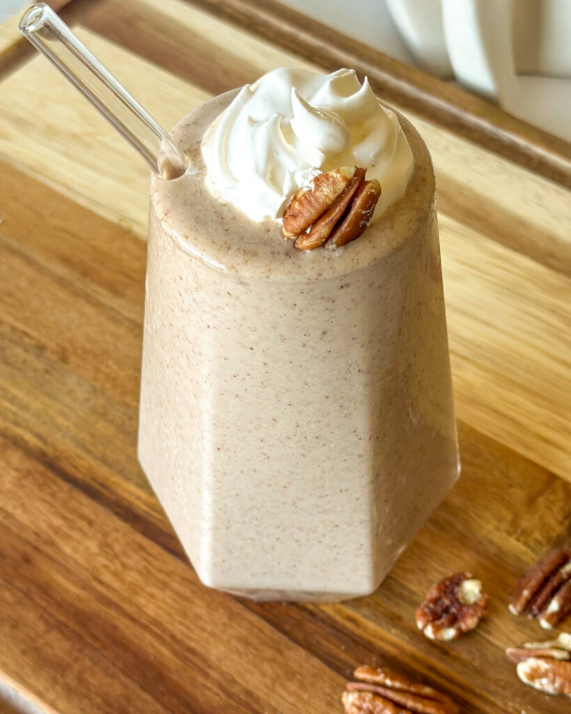 Overhead view of a creamy beige pecan pie smoothie topped with whipped cream and a pecan