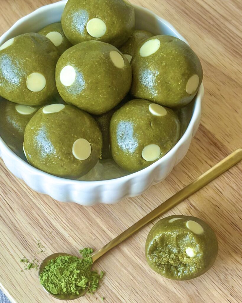 Bowl of vegan matcha cookie dough balls with matcha powder and a bitten cookie dough ball showing the texture