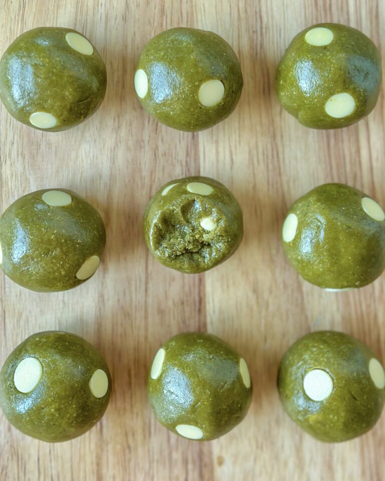 Vegan matcha cookie dough balls arranged in rows with one cut open to show the white chocolate chips inside