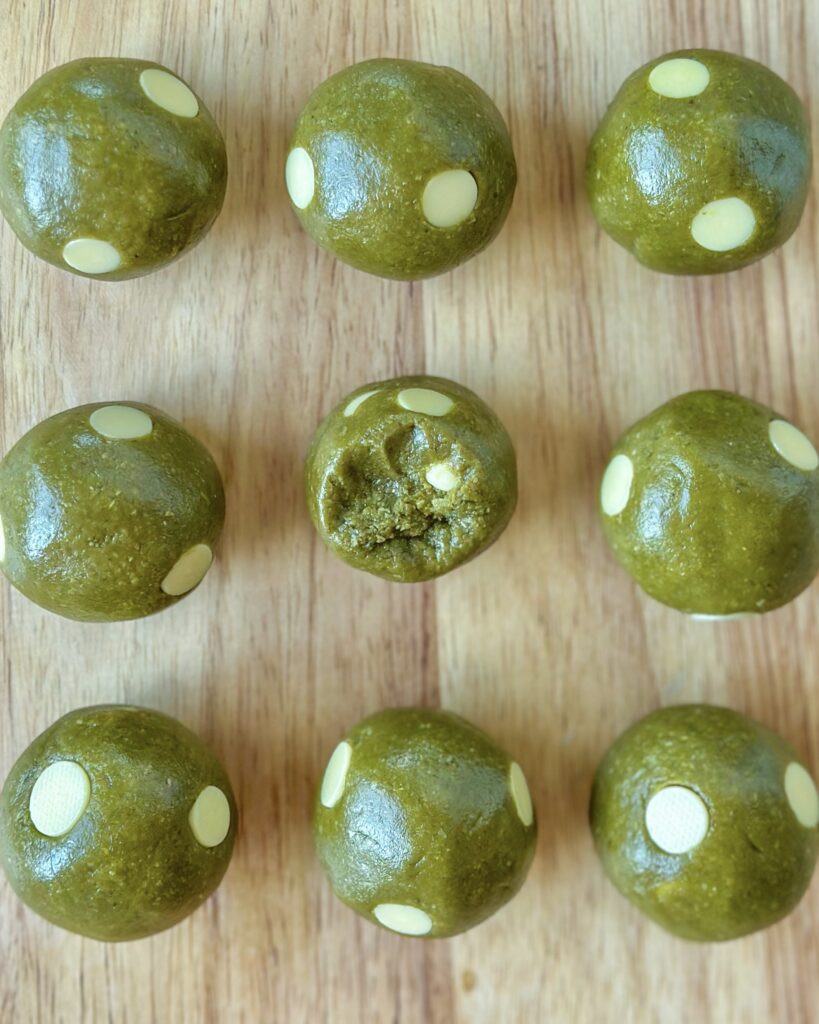 Vegan matcha cookie dough balls arranged in rows with one cut open to show the white chocolate chips inside
