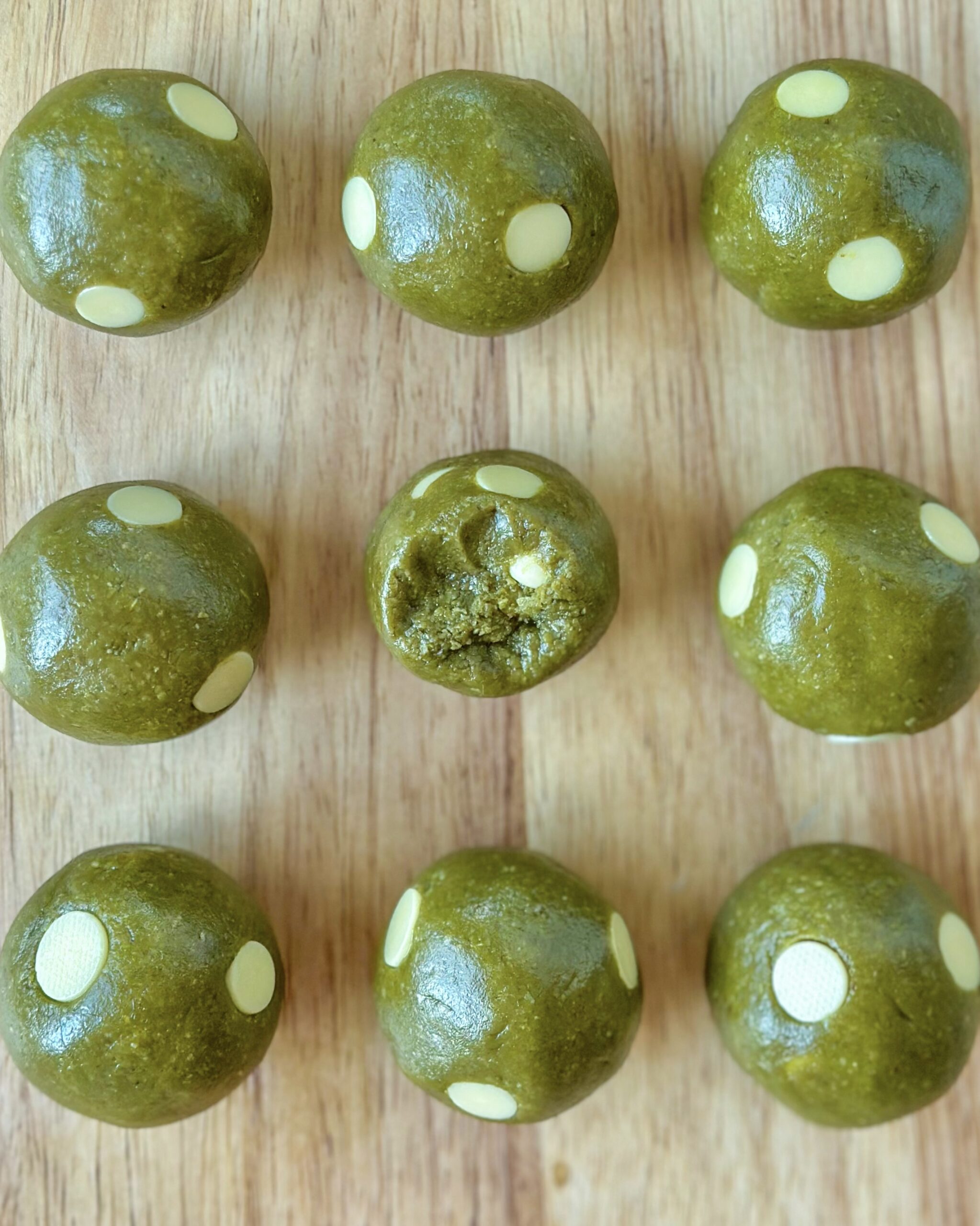 Vegan matcha cookie dough balls arranged in rows with one cut open to show the white chocolate chips inside