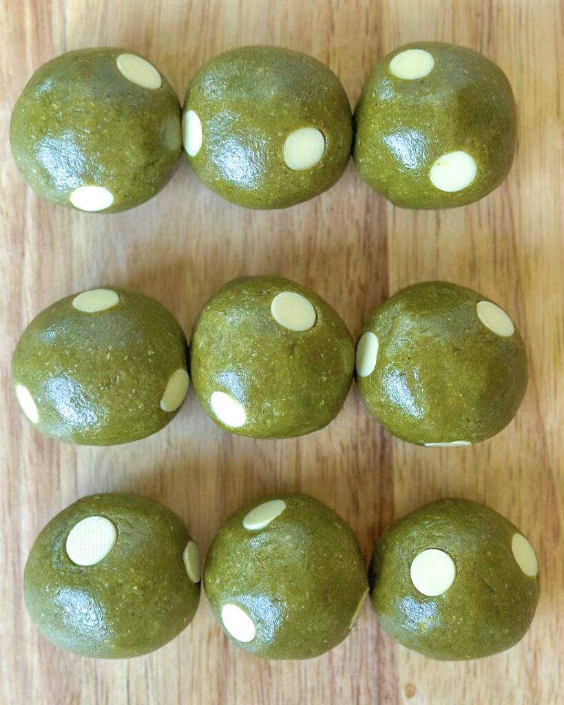 Vegan matcha cookie dough balls lined up in rows with vegan white chocolate chips dotted throughout
